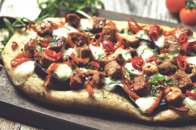 A flatbread pizza topped with cheese, eggplant, pepper, chile, and Quorn Pieces.