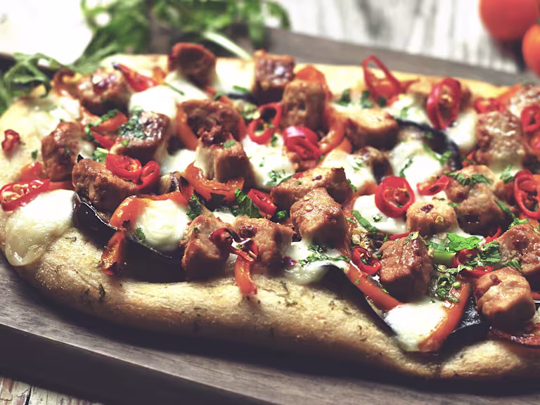 A flatbread pizza topped with cheese, eggplant, pepper, chile, and Quorn Pieces.