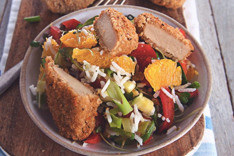 A salad made with lettuce, rice, orange segments, red pepper, cucumber and spring onions topped with Quorn Southern Fried Bites and herbs.