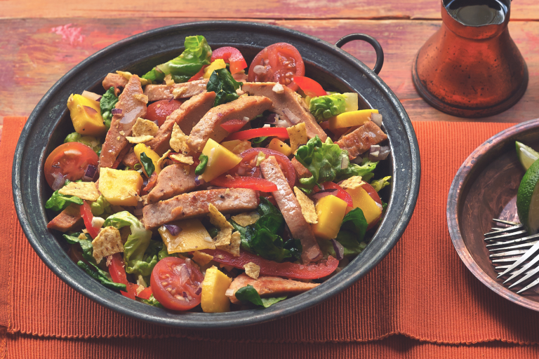 A serving bowl filled with mango salad topped with Quorn Roasted Sliced Fillets.