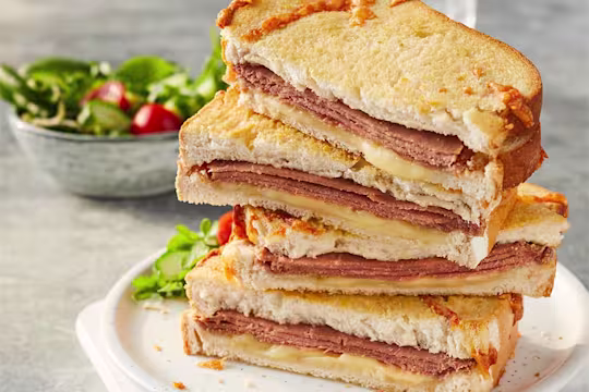 Four Quorn Yorkshire Ham And Cheese Toastie sandwich halves stacked on top of each other to show the filling with a side salad in the back.