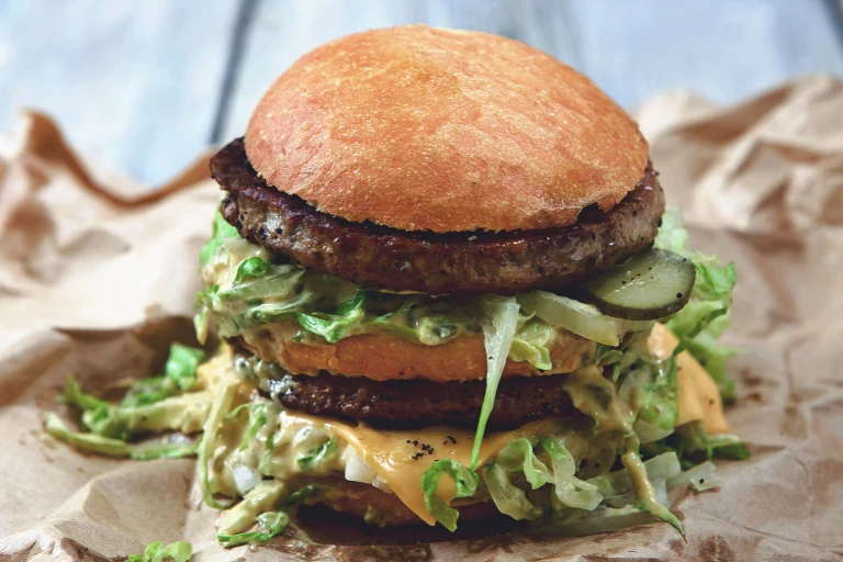 A double-decker burger with Quorn Meatless Gourmet Burgers, cheese, pickles,  shredded lettuce, and plenty of sauce.
