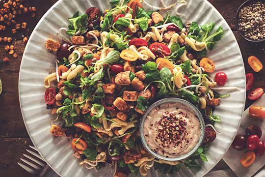 A picnic salad of pasta, black beans, chickpeas, sweetcorn, jalapeno, tomatoes, bean sprouts, and lettuce topped with marinated Quorn Pieces and sunflower seeds.