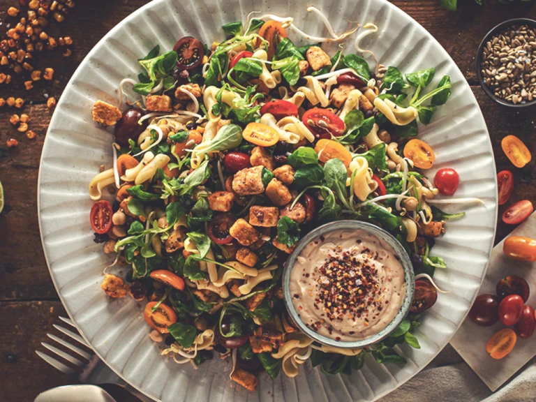 A picnic salad of pasta, black beans, chickpeas, sweetcorn, jalapeno, tomatoes, bean sprouts, and lettuce topped with marinated Quorn Pieces and sunflower seeds.