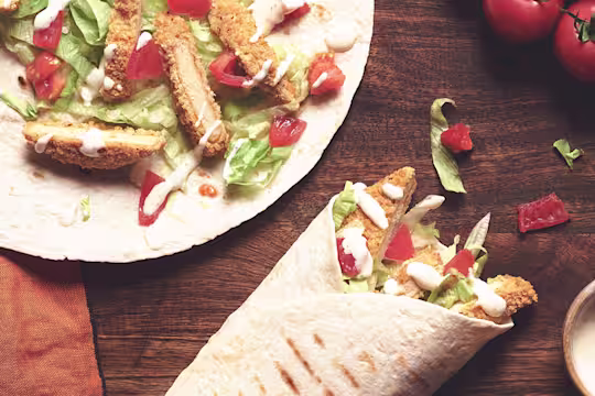 A table set with two Quorn Southern Fried Burger Wraps with a serving of creamy pepper sauce.