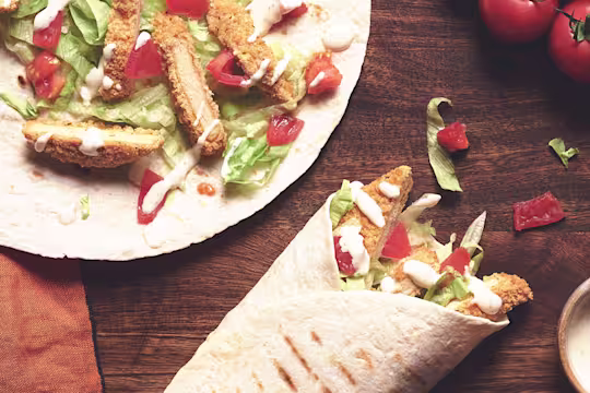 A table set with two Quorn Southern Fried Burger Wraps with a serving of creamy pepper sauce.