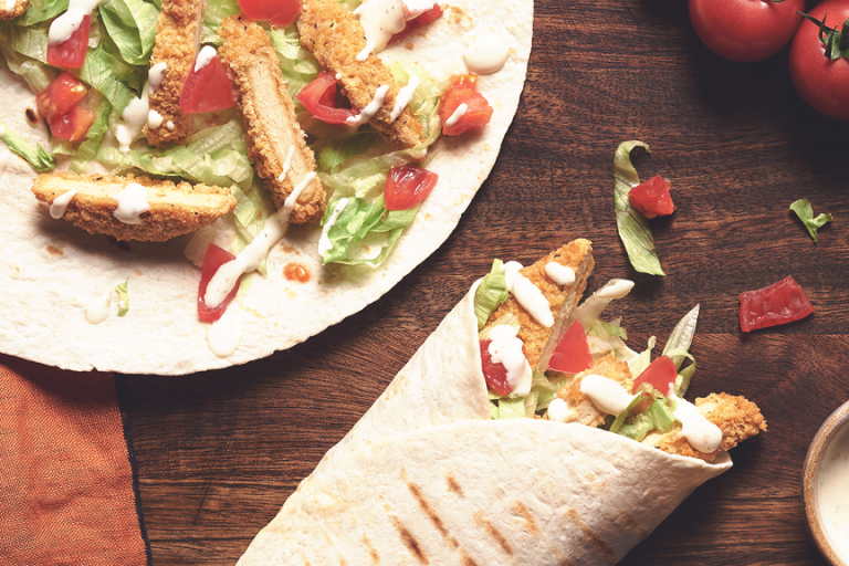 A table set with two Quorn Southern Fried Burger Wraps with a serving of creamy pepper sauce.