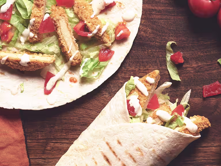 A table set with two Quorn Southern Fried Burger Wraps with a serving of creamy pepper sauce.