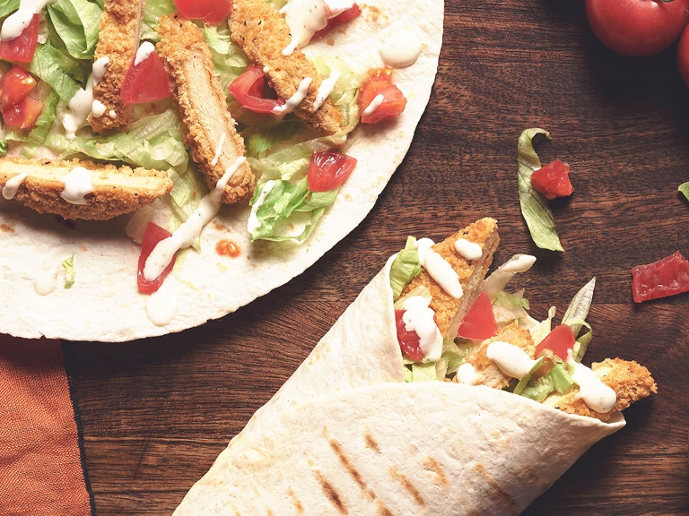 A table set with two Quorn Southern Fried Burger Wraps with a serving of creamy pepper sauce.