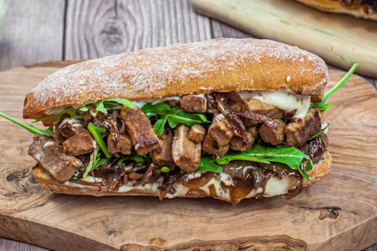 Steak strips and caramelised onions sandwich served on a wooden slab.
