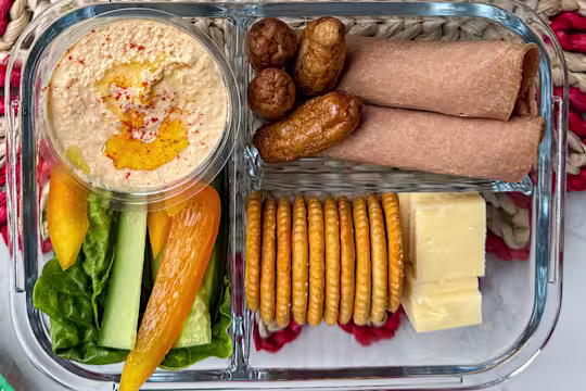 Vegetarian adult lunchbox with Quorn cocktail sausages, wholemeal wraps, cheddar cheese cubes, crackers, hummus, and sliced vegetables