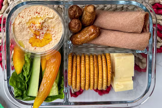 Vegetarian adult lunchbox with Quorn cocktail sausages, wholemeal wraps, cheddar cheese cubes, crackers, hummus, and sliced vegetables