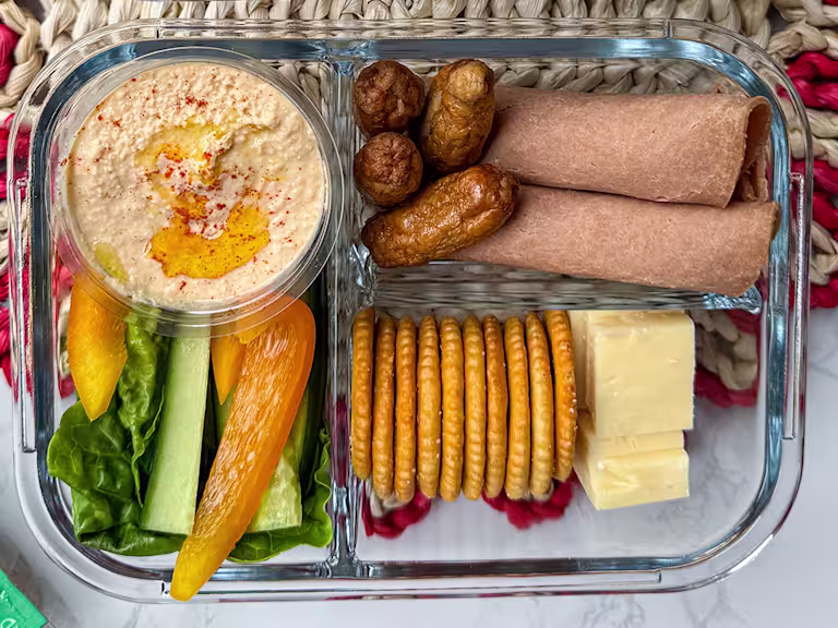 Vegetarian adult lunchbox with Quorn cocktail sausages, wholemeal wraps, cheddar cheese cubes, crackers, hummus, and sliced vegetables