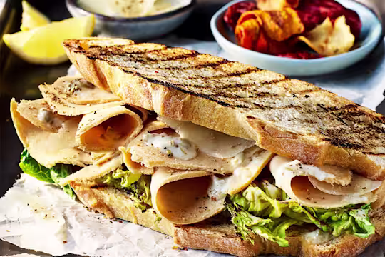 Toasted sourdough bread sandwich with Quorn Vegan Chicken Slices, Caesar dressing and salad leaves with a side of vegetable crisps.