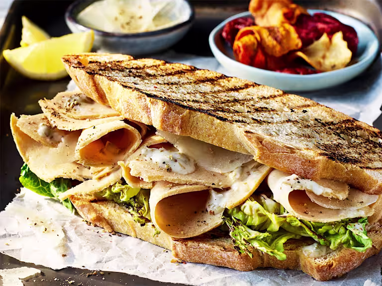 Toasted sourdough bread sandwich with Quorn Vegan Chicken Slices, Caesar dressing and salad leaves with a side of vegetable crisps.