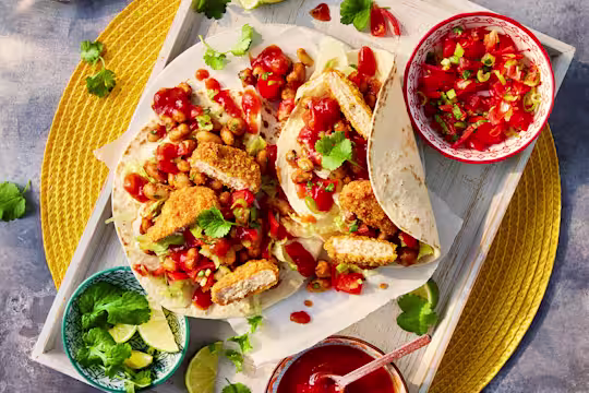 Two vegetarian chicken nugget tacos served with sides of salsa and lime wedges