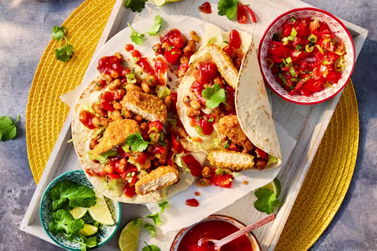 Two vegetarian chicken nugget tacos served with sides of salsa and lime wedges