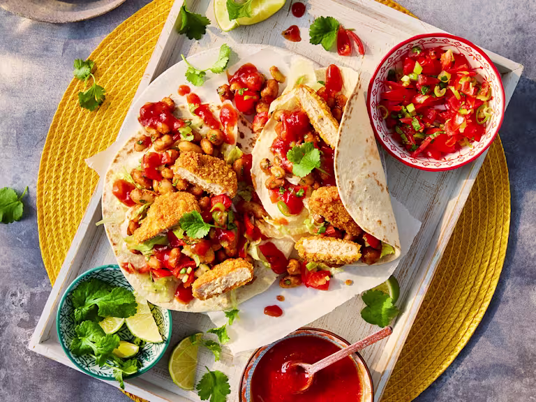 Two vegetarian chicken nugget tacos served with sides of salsa and lime wedges