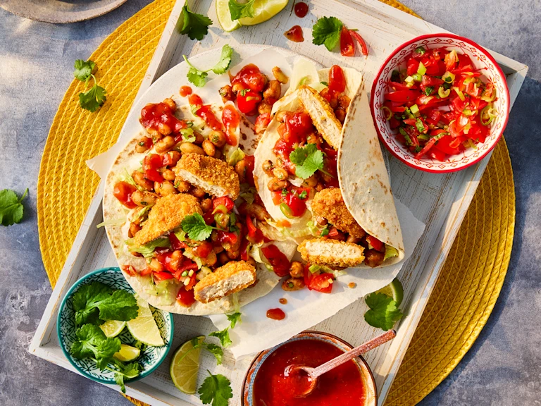 Two vegetarian chicken nugget tacos served with sides of salsa and lime wedges
