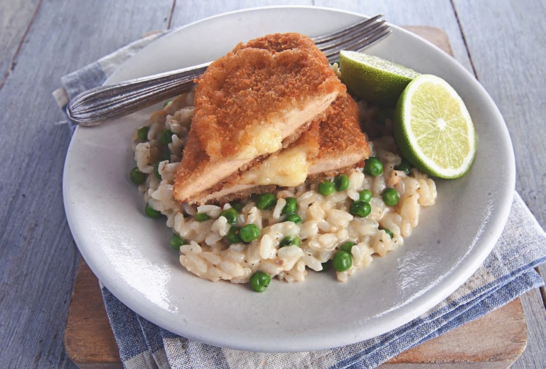 A Quorn Meatless Sharp Cheese Cutlet atop a bed of risotto with green peas, with a halved lime on the side.