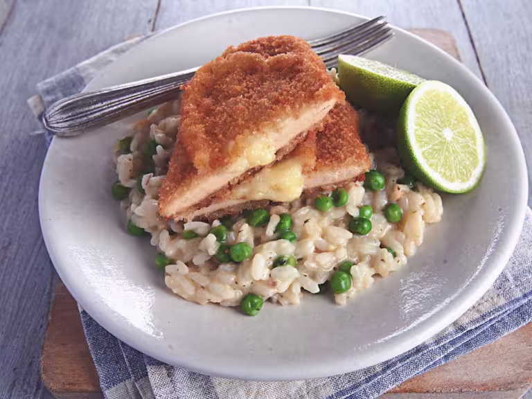 A Quorn Meatless Sharp Cheese Cutlet atop a bed of risotto with green peas, with a halved lime on the side.