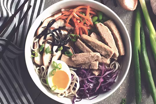 Soup noodles made with Quorn Fillets, carrot, edamame beans, cabbage and half an egg served on top of noodles in a bowl