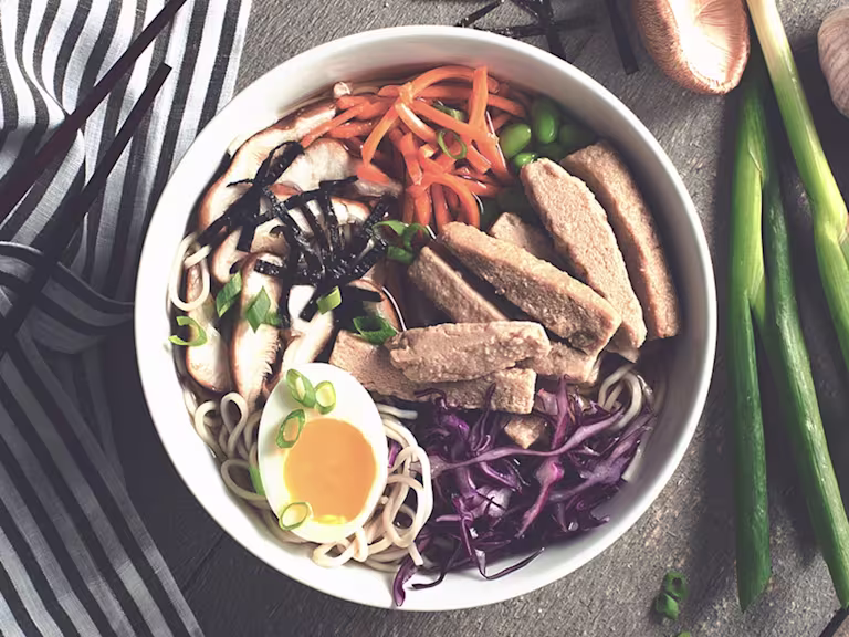 Soup noodles made with Quorn Fillets, carrot, edamame beans, cabbage and half an egg served on top of noodles in a bowl