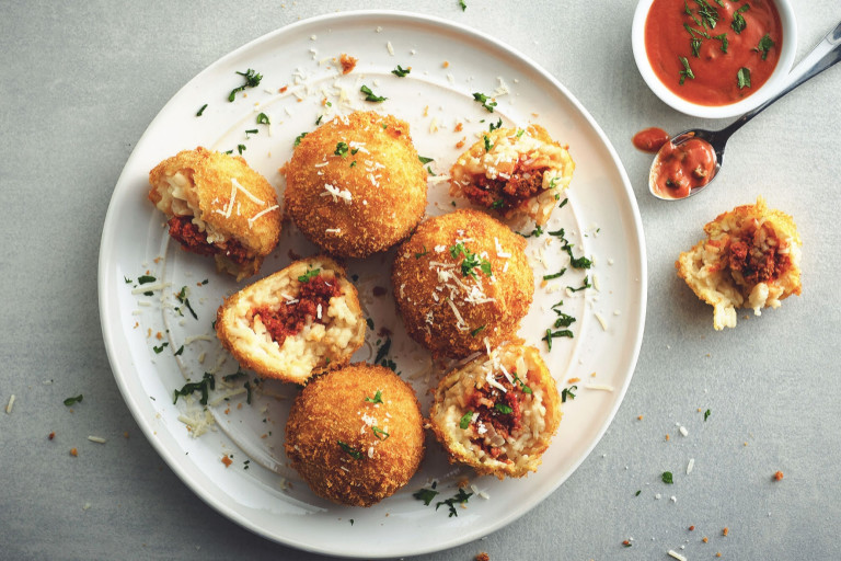 Fried arancini rice balls arranged on a plate with two halved to show a filling of risotto and Quorn Mince.