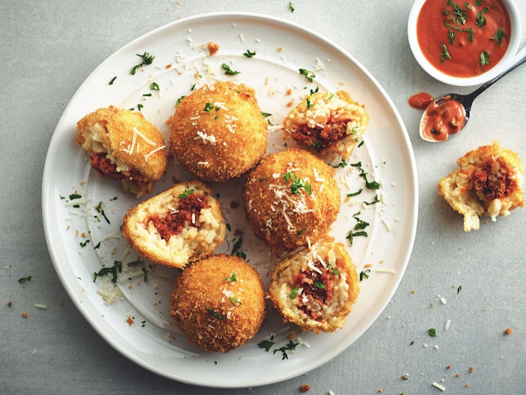 Fried arancini rice balls arranged on a plate with two halved to show a filling of risotto and Quorn Mince.