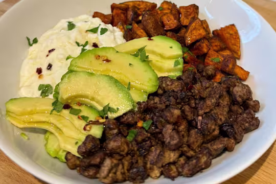 A Hot Honey Cottage Cheese Bowl with Quorn Mince, sliced avocado, parsley and sweet potato in a white bowl.