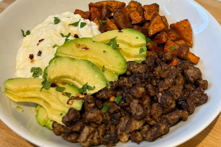 A Hot Honey Cottage Cheese Bowl with Quorn Mince, sliced avocado, parsley and sweet potato in a white bowl.