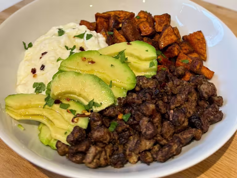 A Hot Honey Cottage Cheese Bowl with Quorn Mince, sliced avocado, parsley and sweet potato in a white bowl.