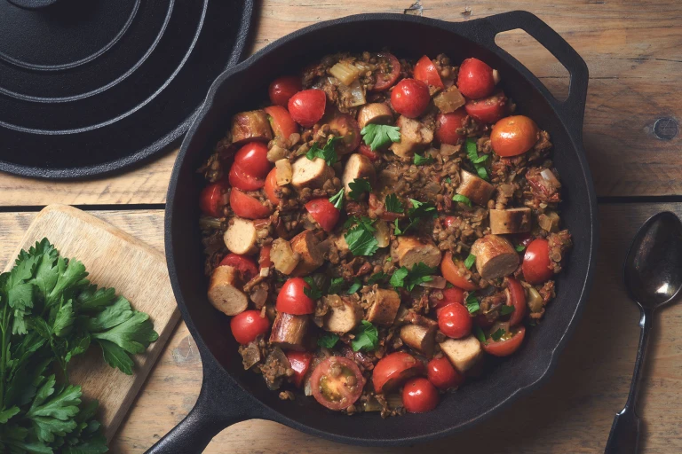 A lentil salad made with Quorn Sausages and tomatoes topped with parsley in a skillet.