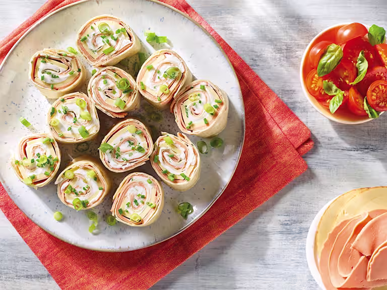 Eleven slices of a vegan ham and cheese roll made with Quorn Vegan Smoky Ham Free Slices, Violife Smoky Cheddar Flavour Slices, Violife Creamy, and chives topped with sliced spring onions.