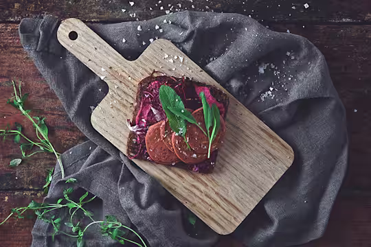 Vegan recipe made with a slice of rye bread topped with Quorn Vegan Pepperoni dressed with herbs served on a chopping board