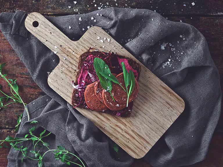 Vegan recipe made with a slice of rye bread topped with Quorn Vegan Pepperoni dressed with herbs served on a chopping board
