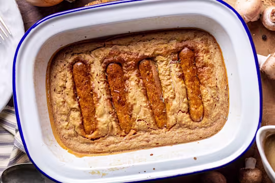 Vegan toad in the whole served in a dish with gravy and mushrooms on the side.