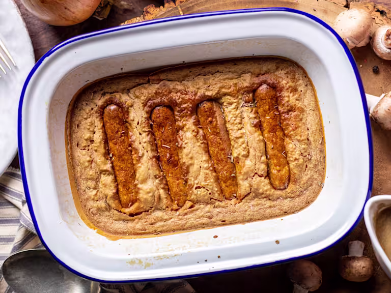 Vegan toad in the whole served in a dish with gravy and mushrooms on the side.
