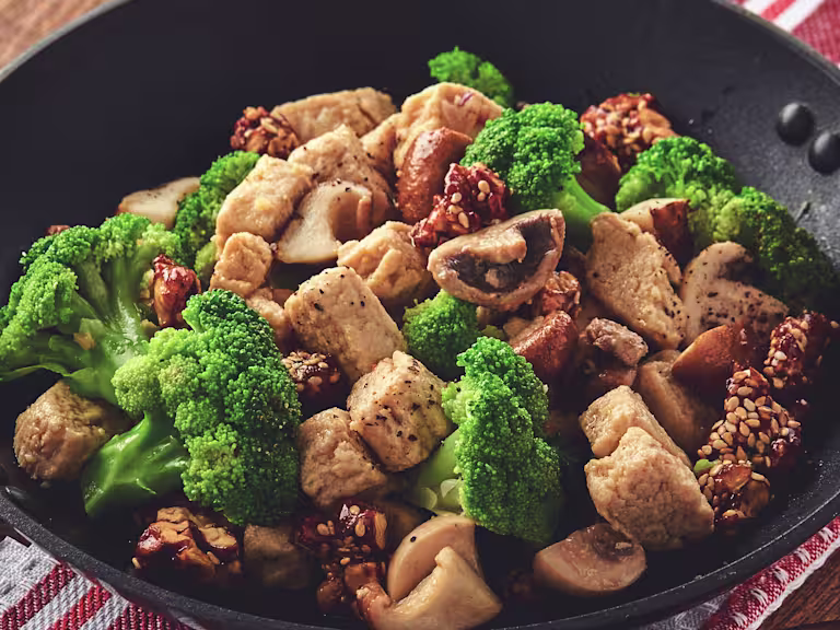 A skillet filled with a stir fry of Quorn Pieces, broccoli, mushrooms, and candied walnuts.