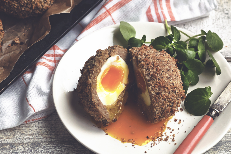 A Scotch egg sliced in half to reveal a soft-cooked egg wrapped in Quorn Sausage and breadcrumbs.