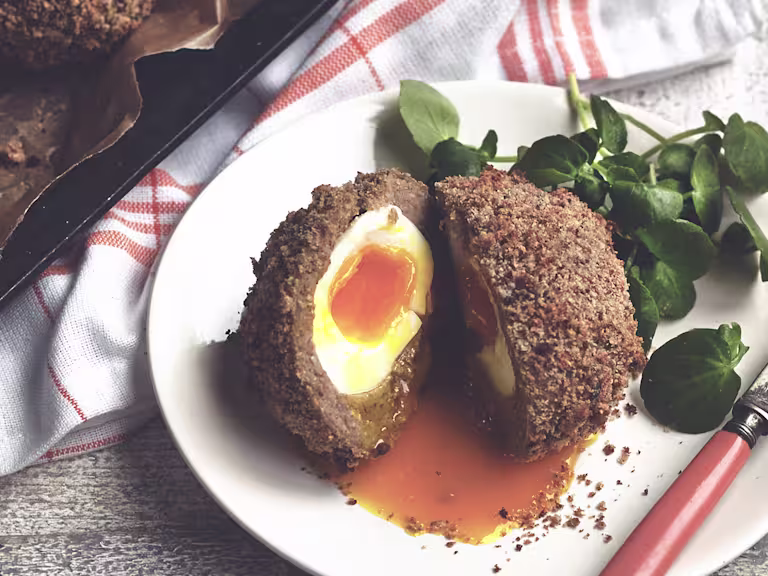 A Scotch egg sliced in half to reveal a soft-cooked egg wrapped in Quorn Sausage and breadcrumbs.