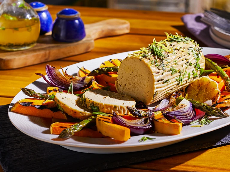 A summer vegetarian roast made with Quorn Meatless Roast topped with rosemary and lemon zest in the centre of a platter surrounded by roasted vegetables.