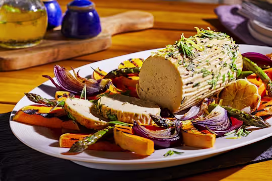 A summer vegetarian roast made with Quorn Meatless Roast topped with rosemary and lemon zest in the centre of a platter surrounded by roasted vegetables.