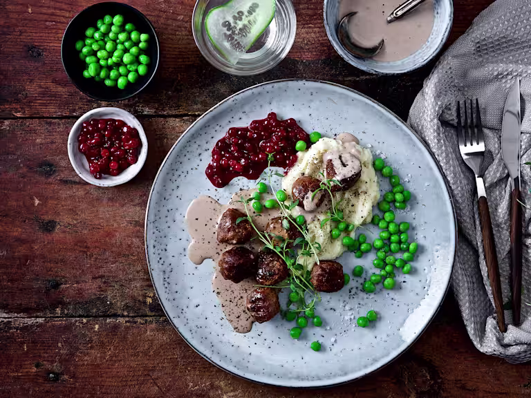 Veganska köttbullar med mos, gräddsås och rårörda lingon på tallrik.