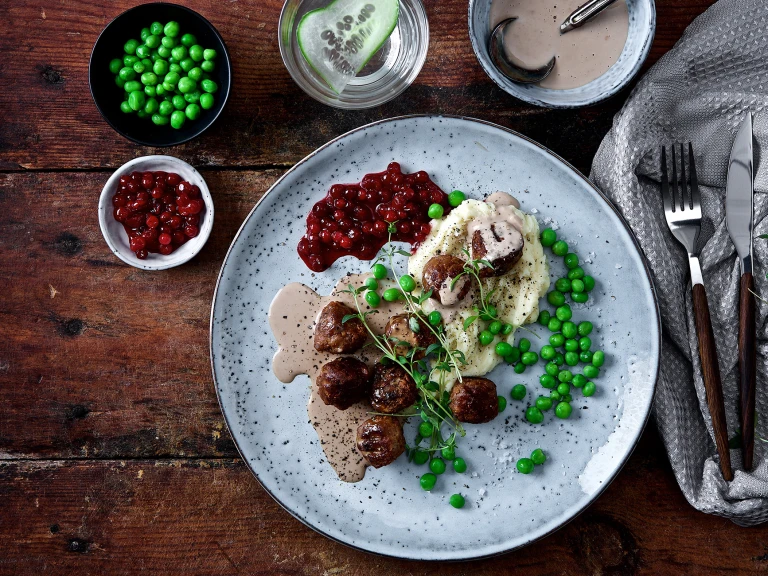 Veganska köttbullar med mos, gräddsås och rårörda lingon på tallrik.