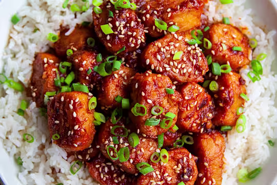 A bowl of vegetarian sticky sesame chicken made using Quorn Pieces served on top of a bowl of rice.