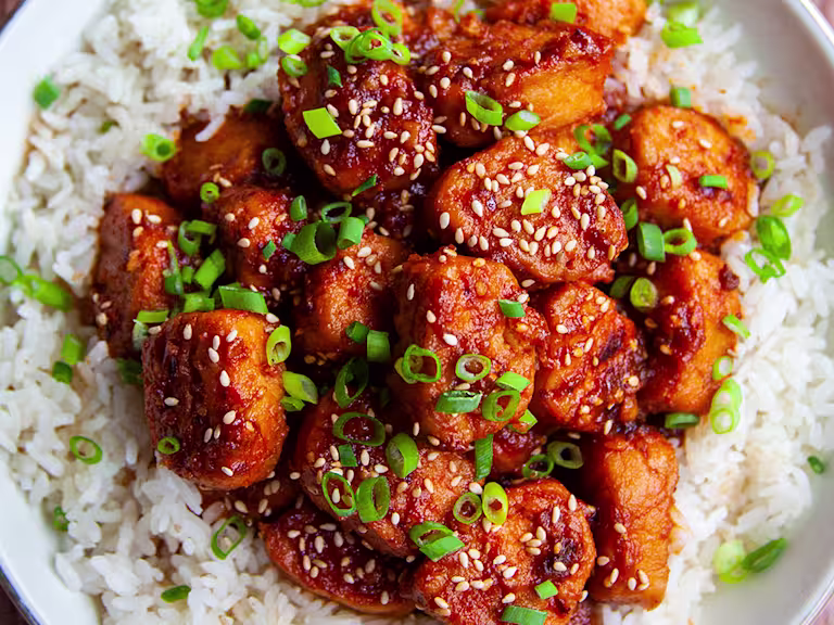 A bowl of vegetarian sticky sesame chicken made using Quorn Pieces served on top of a bowl of rice.