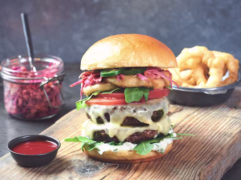 A Fresh and Spicy Quorn Burger sat beside a bowl of onion rings and a jar of coleslaw.