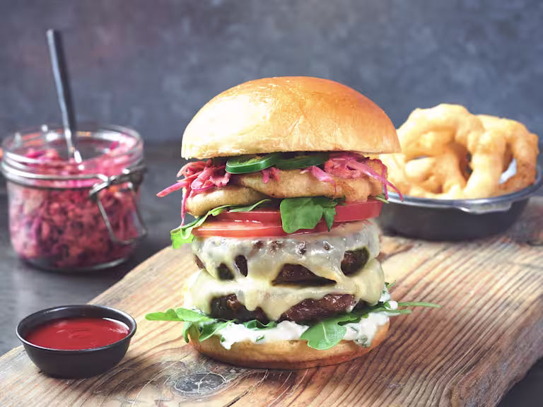 A Fresh and Spicy Quorn Burger sat beside a bowl of onion rings and a jar of coleslaw.