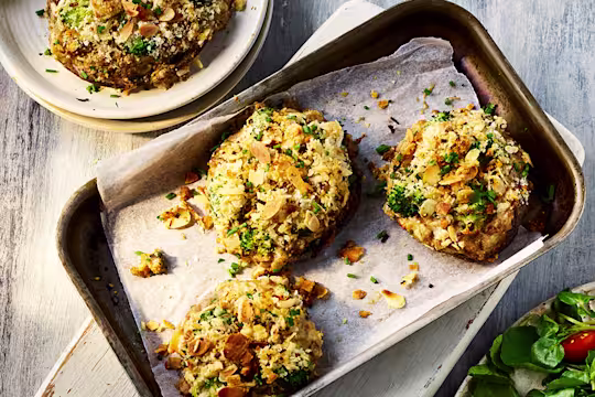 Four stuffed peppers topped served on a baking tray and a white dish with a side salad.